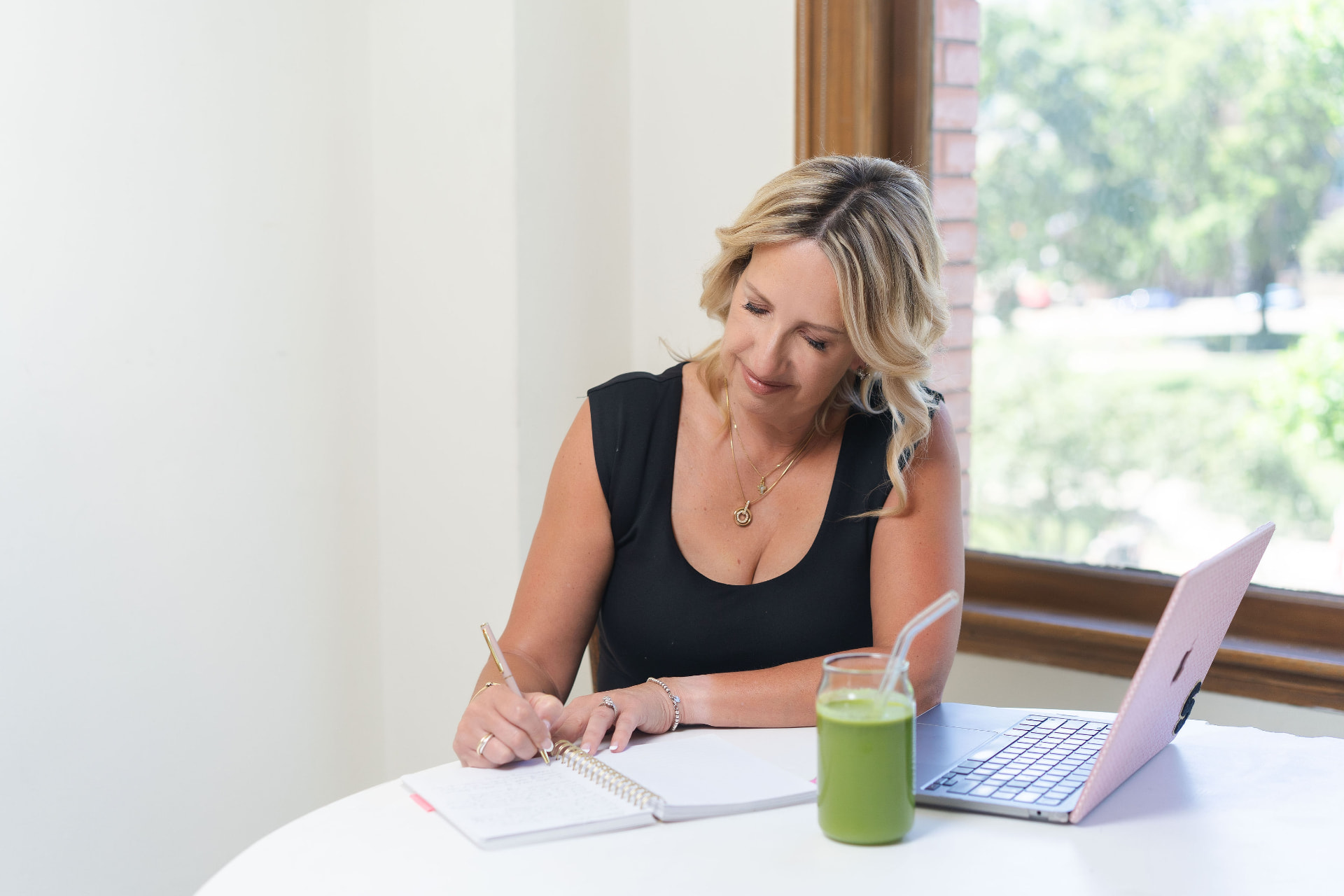 Susan writing notes in a journal beside a green smoothie and laptop
